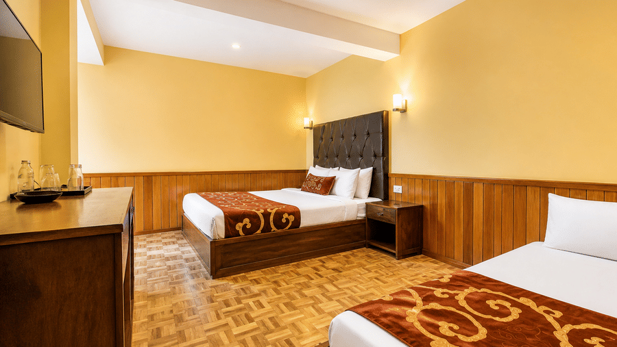 Beds are arranged on the floor of the Family Room at Orsino Khangri Karpo Retreat & Spa, Lachung. A television and a chest of drawers stand against the wall. Lights are mounted above the beds.