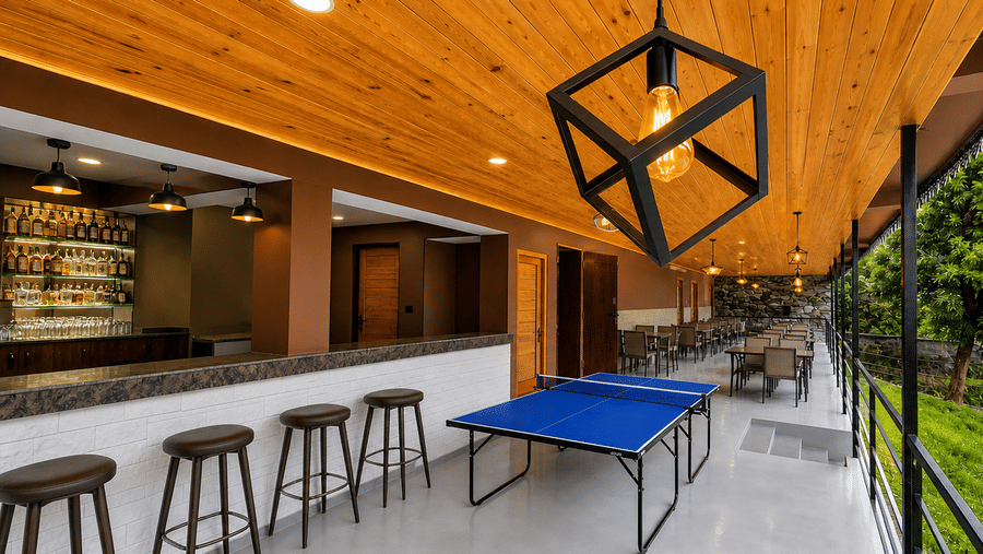Opal bar at Orsino Khangri Karpo Retreat & Spa, Lachung featuring a counter with stools sits next to a table tennis table. The ceiling is wood with a modern light fixture.
