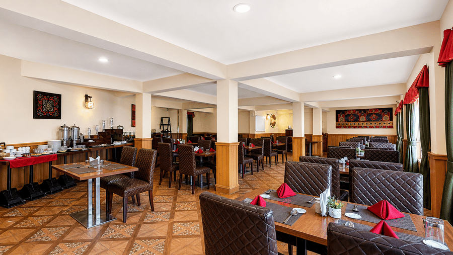 Orion restaurant at Orsino Khangri Karpo Retreat & Spa, Lachung featuring multiple set tables fill a room with pillars and tiled floors. A buffet station is positioned against a wall.