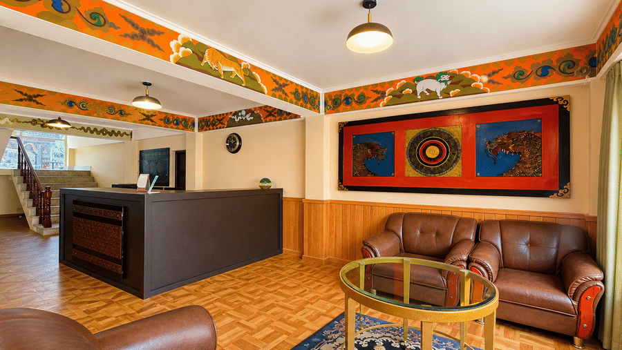A lounge area within Orsino Khangri Karpo Retreat & Spa, Lachung featuring sofas, a table, and decorative patterns along the ceiling borders.