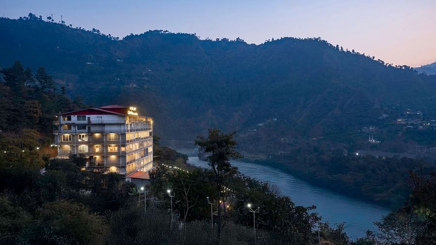 Facade of SPT Clarks Inn, Mandi lit up next to the Beas River with a silhouette of mountains as the sun is setting