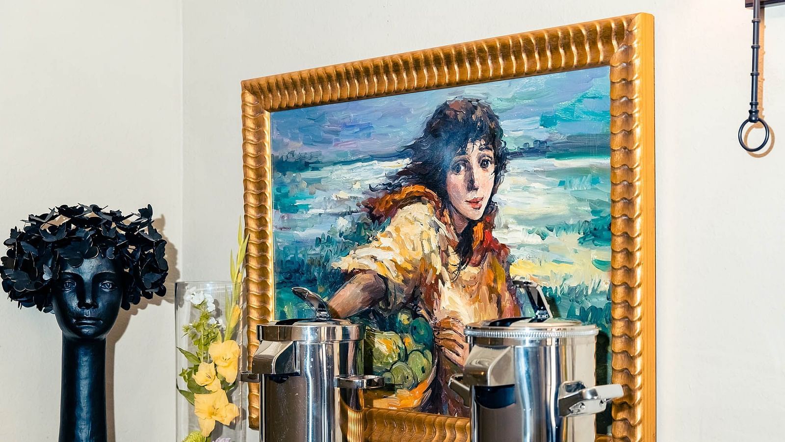 A framed painting of a woman  hangs above a table, with a vase of flowers nearby.- The Grand Hotel & Ballroom, McKinney