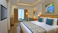 Premium King Room at Golden Sarovar Portico, Amritsar featuring a double size bed, a cabinet table, a sofa chair and a work station.