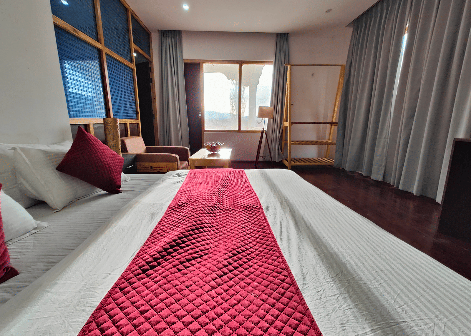 A large suite featuring a quilted red bed runner and soft grey curtains at Indus Serenity Retreat.