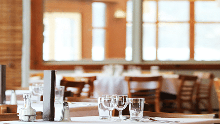 A bright and airy dining area with neatly set tables and wooden furniture, creating a welcoming atmosphere.