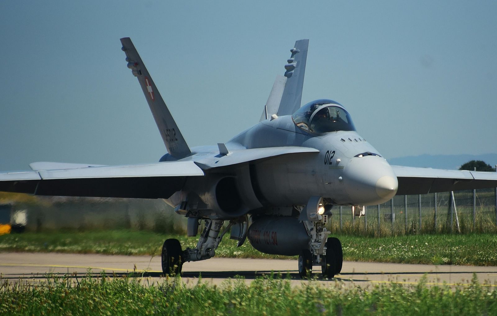 Front view of a fighter jet on an airfield, with visible details like the cockpit, wings, and landing gear.