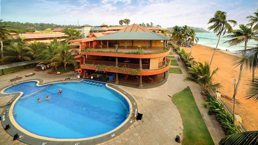 Uday Samudra Leisure Beach Hotel offers a swimming pool, tall buildings, swaying palm trees, and a sandy beach set against a clear blue sky