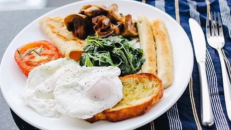 Plate of English breakfast with poached eggs, toast, spinach, mushrooms, and tomatoes.