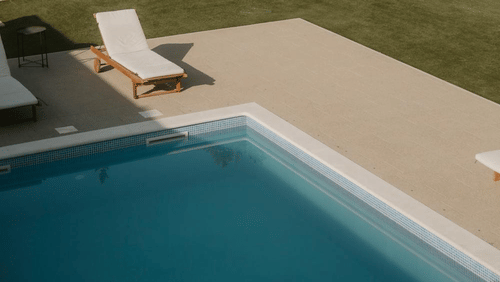 A poolside view with lounge chair, paved area, and trees in the background.