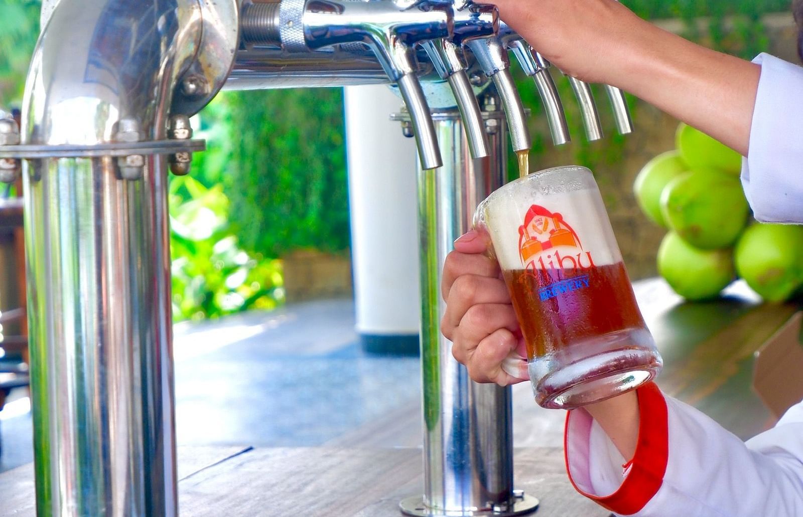 A person filling up a beer in a glass with the logo of the hotel on it - Alibu Resort Nha Trang