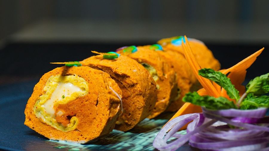 Skewered food with garnish on a dark plate, presented with sliced rings and herbs.