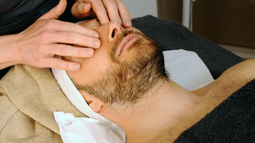 A man receiving facial massage from a masseur