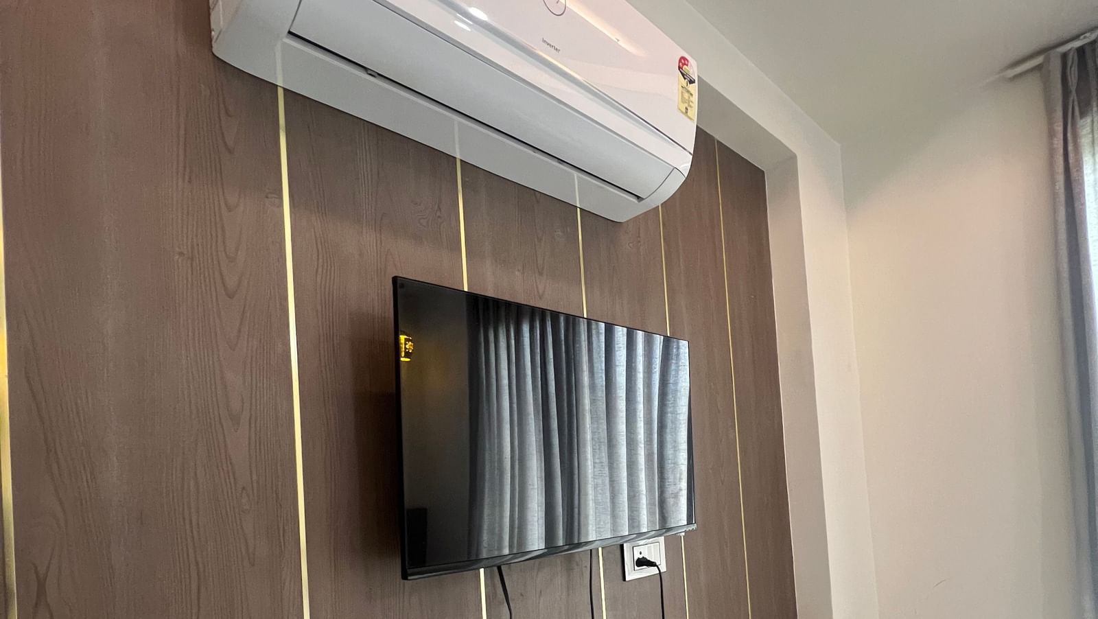 Wall-mounted TV right below the wall-mounted AC in the Daksh Bliss room at Daksh The Valley Resort, Saputara.