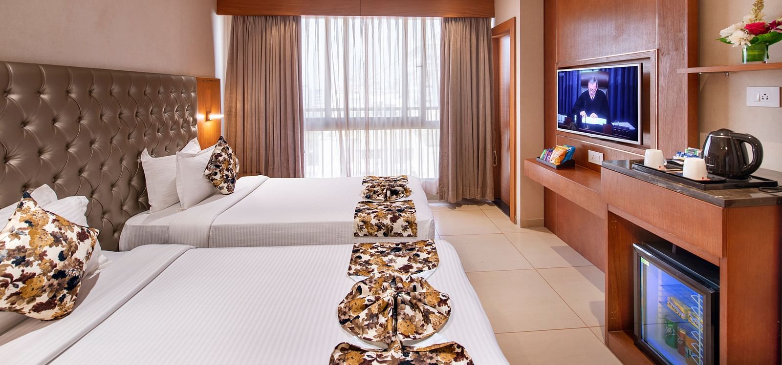A hotel room with twin beds and a television unit - SK Lords Inn Ahmedabad