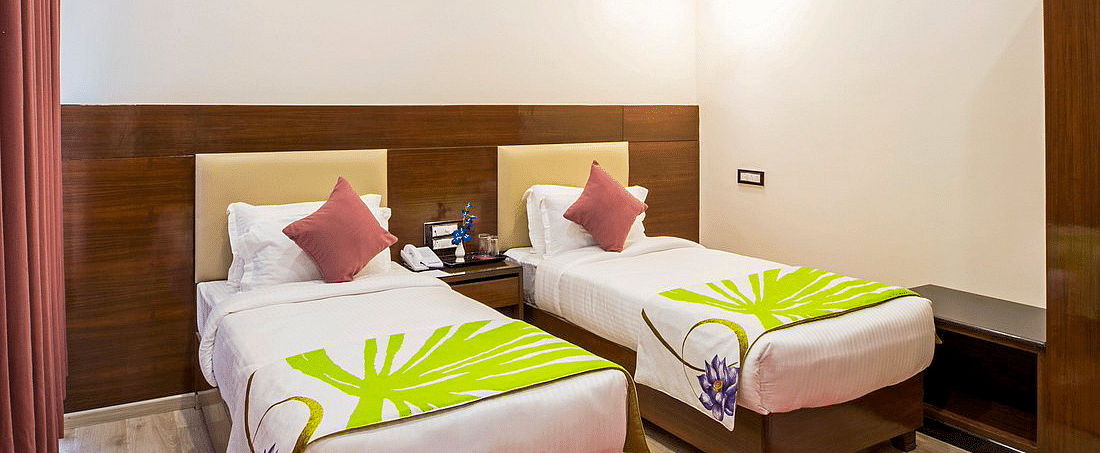 Corner view shot of the Deluxe Twin Room at Regenta Inn DLS featuring two single beds along with a bright red carpet on the floor.