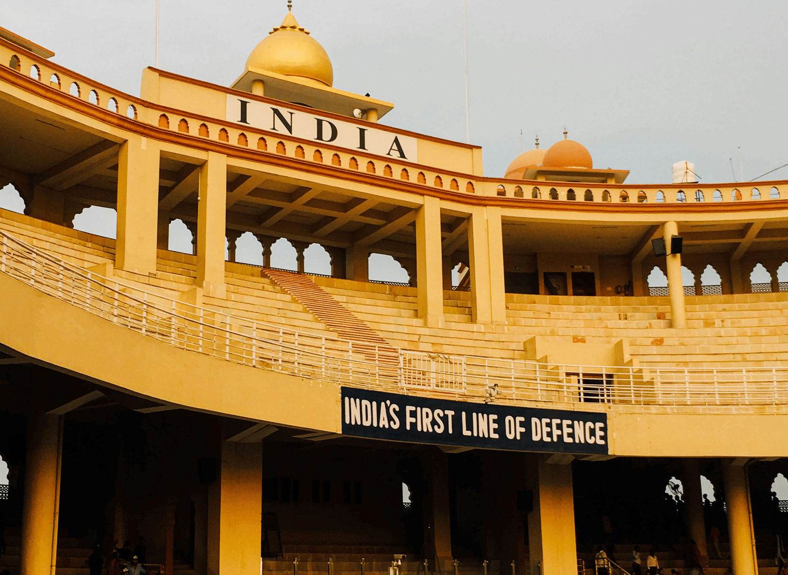 The exterior of a large, semi-circular stadium at the Attari-Wagah Border, with crowds of people visible in the lower sections