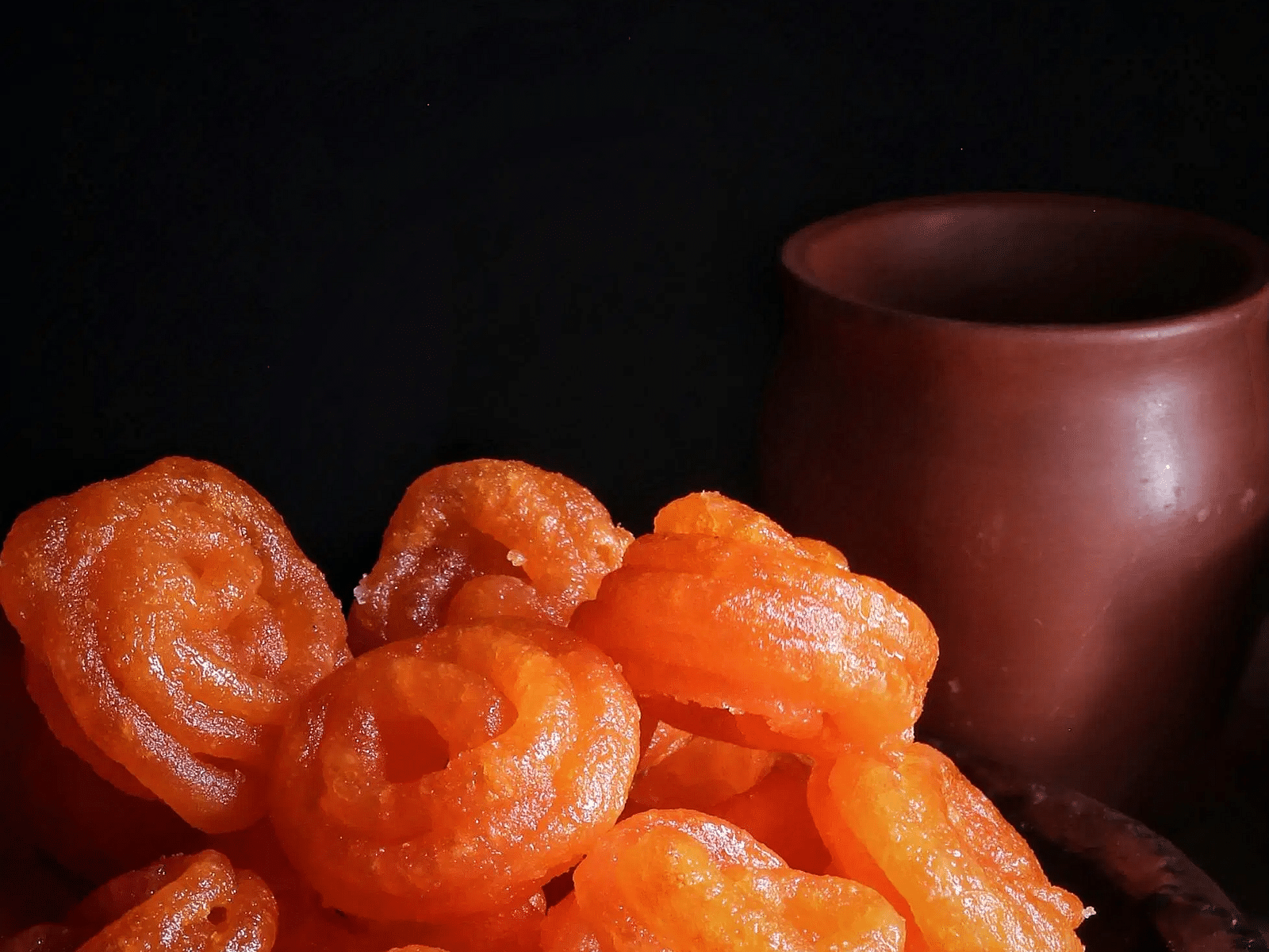 Plate of hot, freshly made jalebis with an earthen cup in the background.