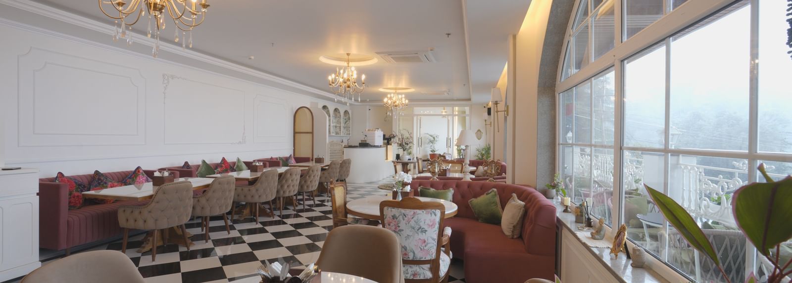Sun-lit dining area with chandeliers, white tables, and cushioned booths - Mayfair Cafe & Suites, Dalhousie