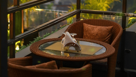 2 chairs facing each other on a terrace with warm lights besides it on a late evening.