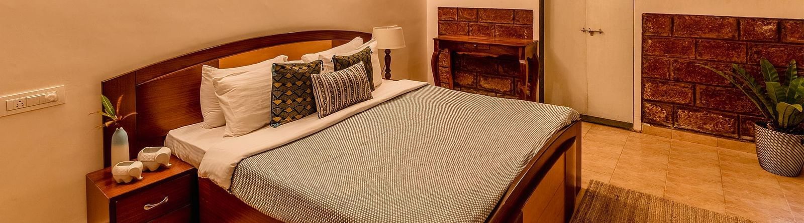 A double bed room with a side table with amenities, lights, ceiling fan, wooden floor and door