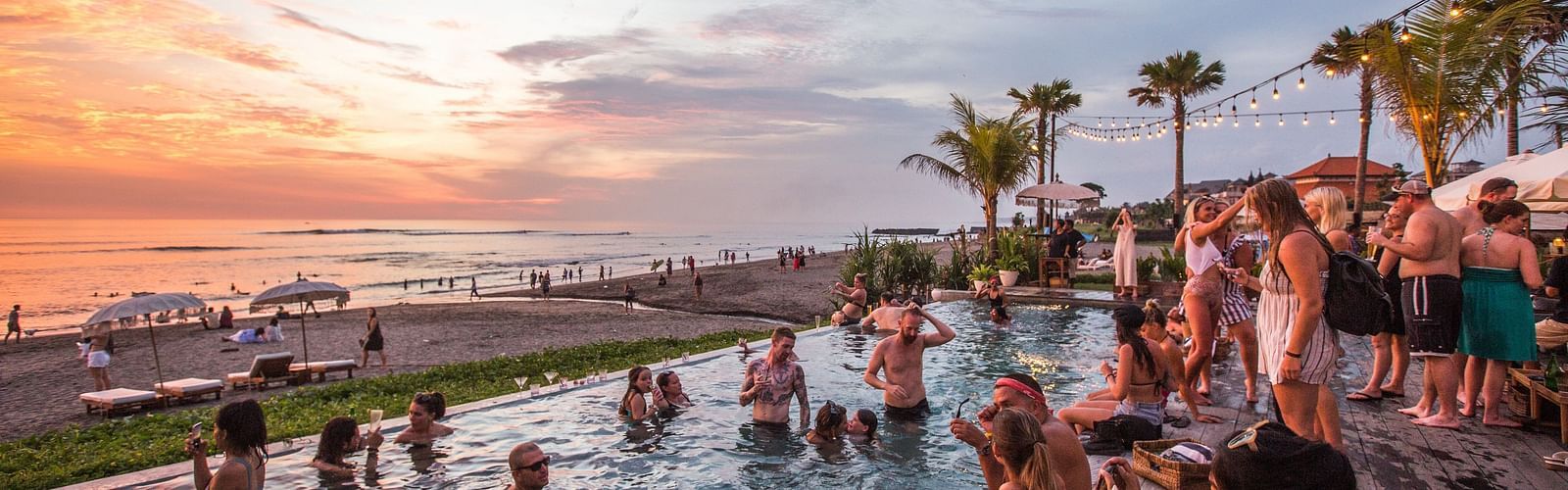 a crowd of people enjoying by dipping into the pool and looking at the sunset in the background