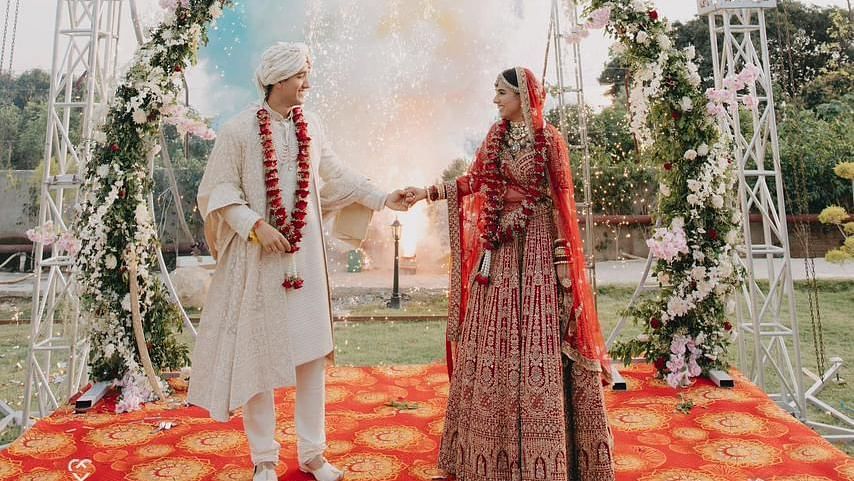 A bride and groom exchanging vows under a floral archway, with colorful drapes in the background.