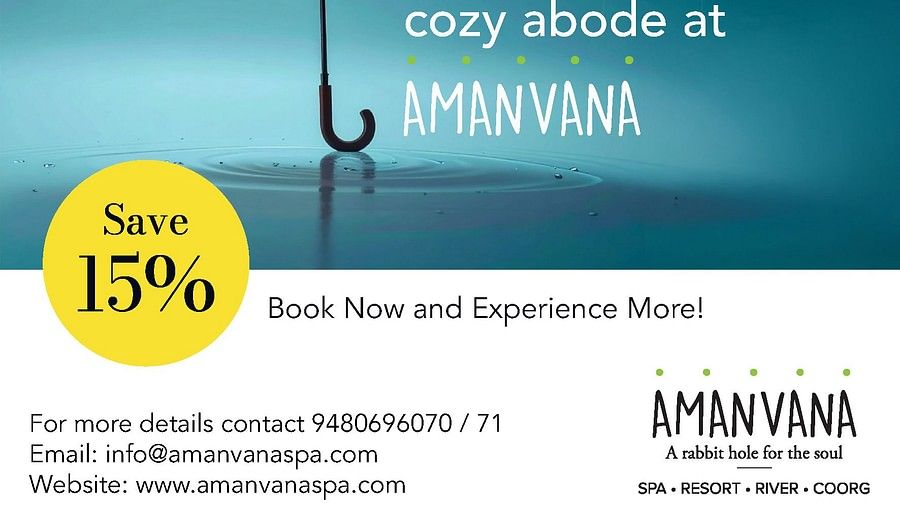 Orange umbrella in rain with water droplets against blue sky, advertising Amanvana Spa Resort, Coorgs monsoon experience with 15% discount offer