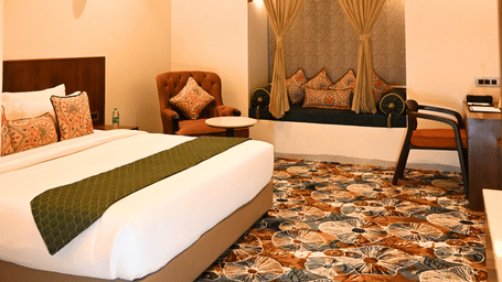 A guest room at Kadamb Kuteer featuring king bed with white linens, patterned cushions, tiled floors, and a seating area by the window.