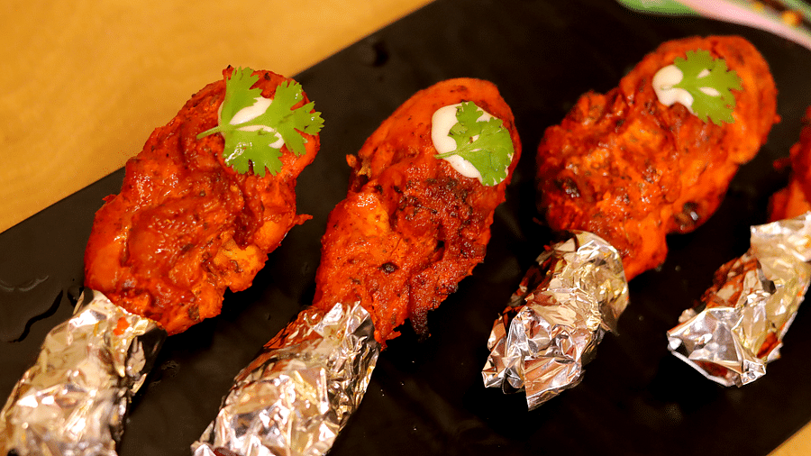 Tandoori chicken drumsticks garnished with cilantro leaves served on a black platter at Themis Barbecue House - Themis Barbecue House, Ambience Mall, Gurugram