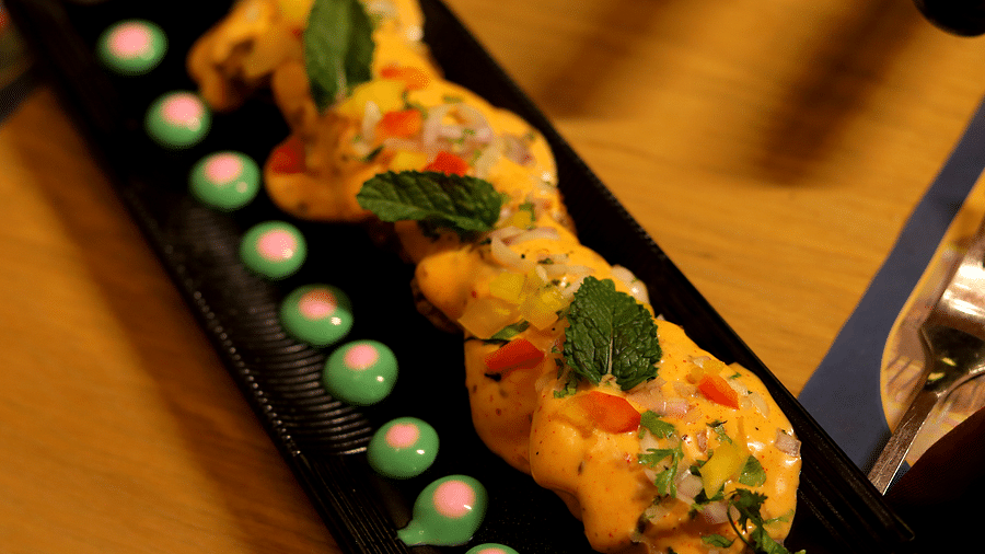 Creamy topped rolls decorated with a herb and dots of green and red sauce on a long rectangular plate - Themis Barbecue House, Ambience Mall, Gurugram