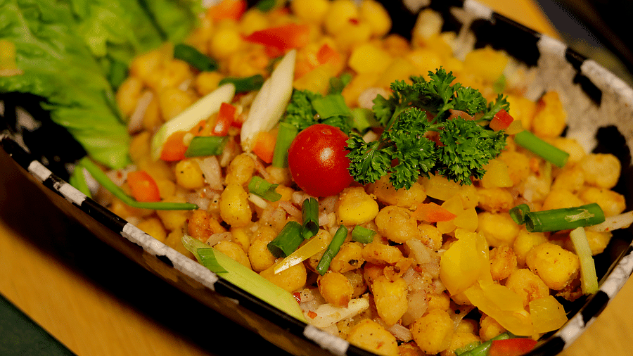 A refreshing chickpea salad with a mix of vegetables in a black dish, garnished with a cherry tomato at Themis Barbecue House, Ambience Mall, Gurugram