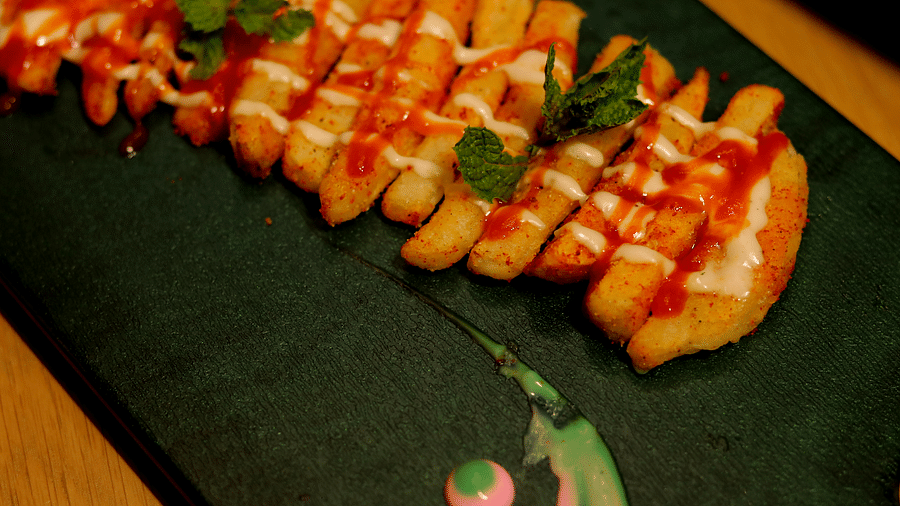 Fried fish fillets drizzled with red sauce and a mint garnish on a green rectangular plate at Themis Barbecue House, Ambience Mall, Gurugram