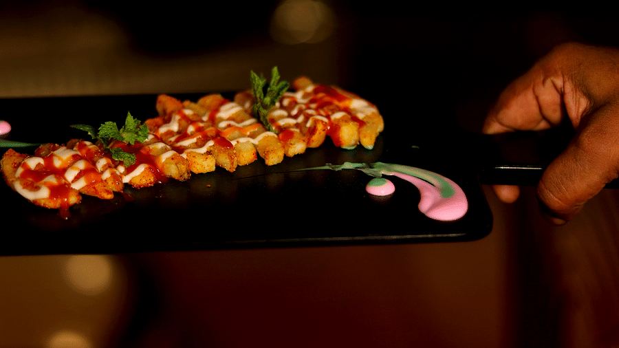 A person presenting a skewer of diced and seasoned chicken with artistic sauce decor at Themis Barbecue House, Ambience Mall, Gurugram
