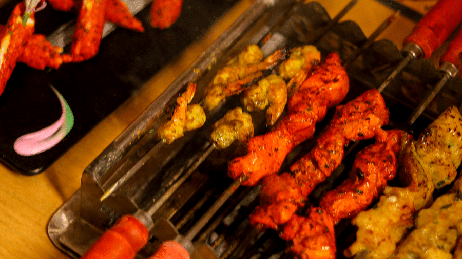 Various skewers of marinated meats over a grill with bamboo handles at Themis Barbecue House, Ambience Mall, Gurugram