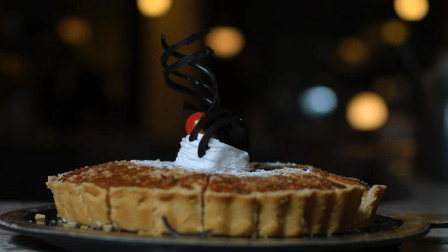 A beautifully arranged fruit tart topped with a chocolate decoration on a dark plate at Themis Barbecue House, Ambience Mall, Gurugram