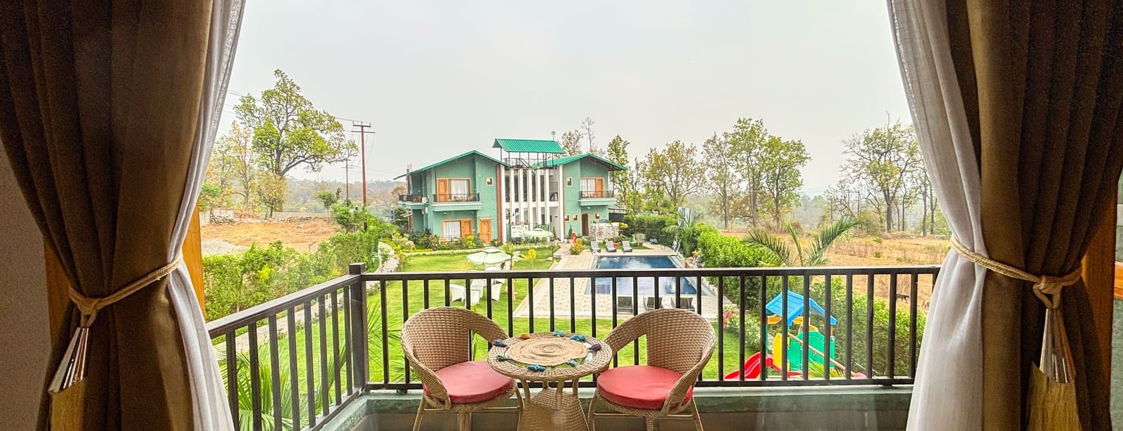 Balcony with seating area overlooking greenery at Corbett Nirvana Resort.