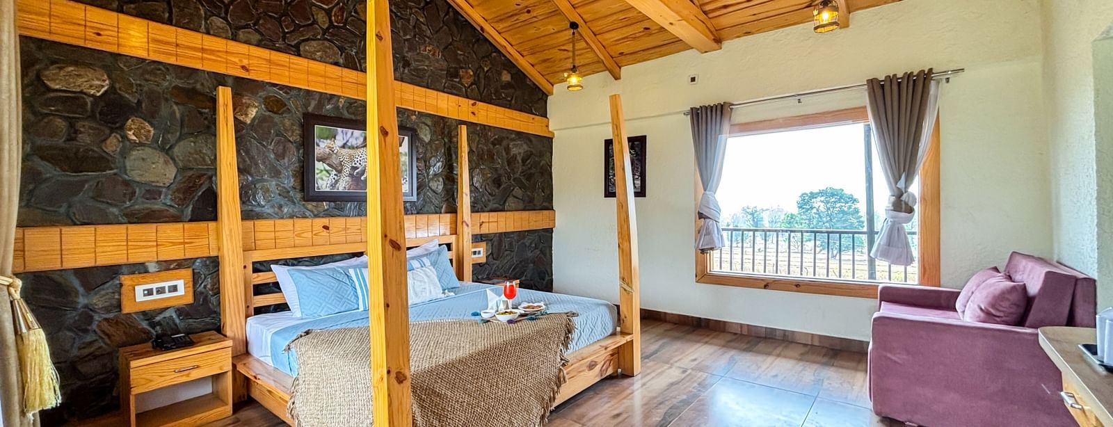 Bright bedroom with canopy bed, wooden ceiling, and balcony access at Corbett Nirvana Resort.