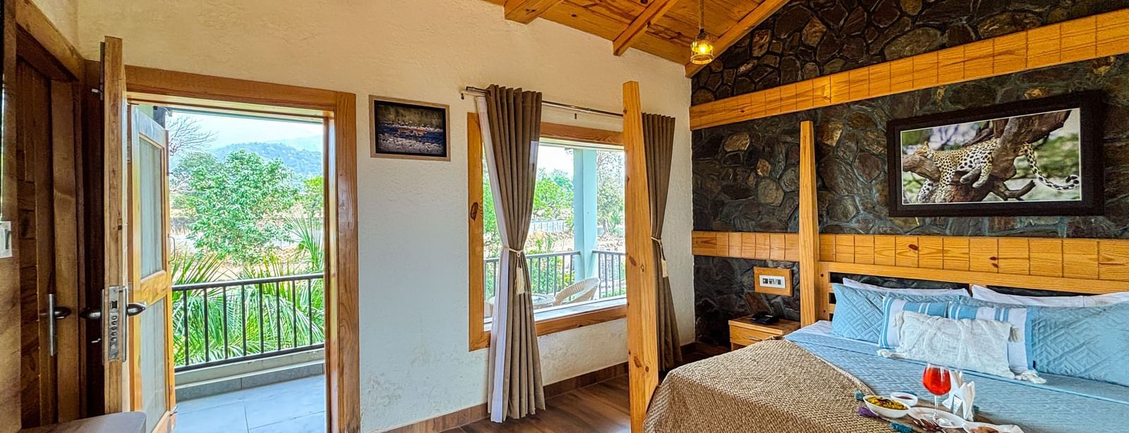Spacious resort room with wooden ceiling, large windows, and balcony at Corbett Nirvana Resort.
