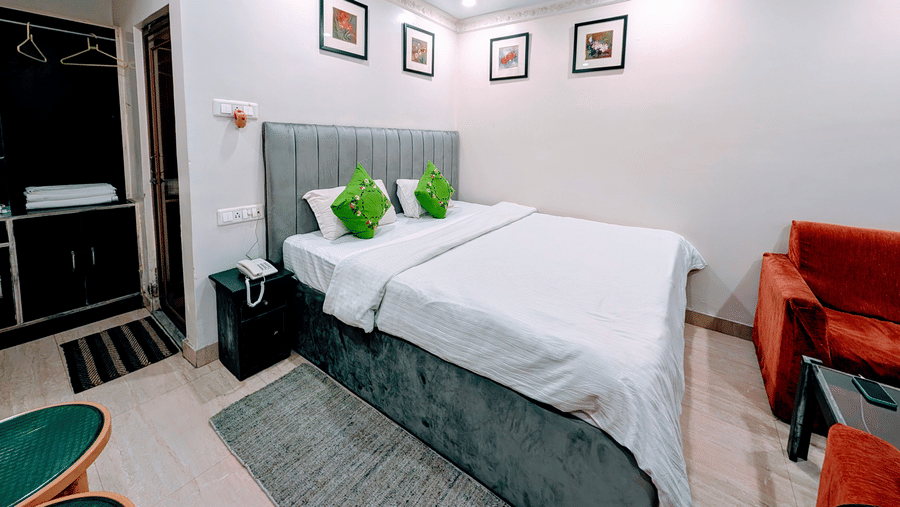 A neat hotel room featuring a double bed dressed in white linen with bright green accent cushions and a grey headboard.