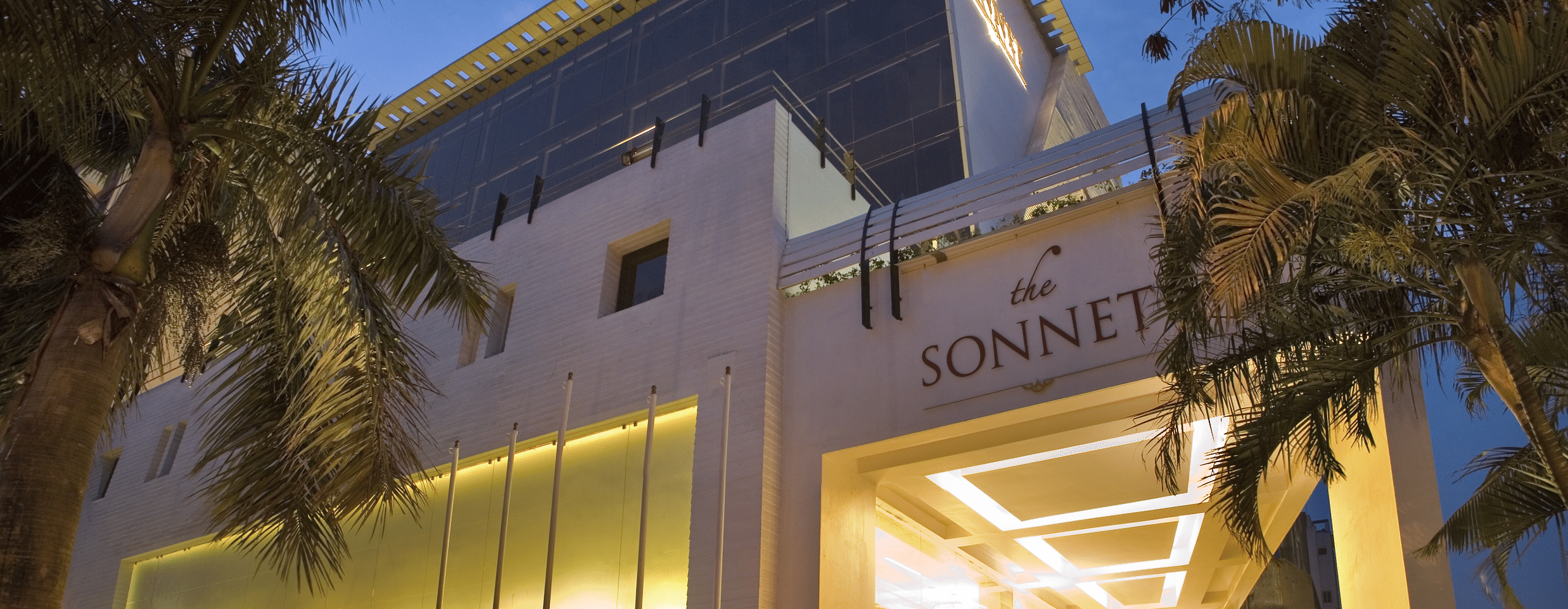 The illuminated exterior of a hotel entrance at night, with palm trees and a sign that reads 'The Sonnet'.