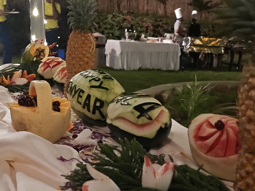A vertical close-up of a table laden with floral decorations, possibly at an outdoor event, with blurred lights and greenery in the background.