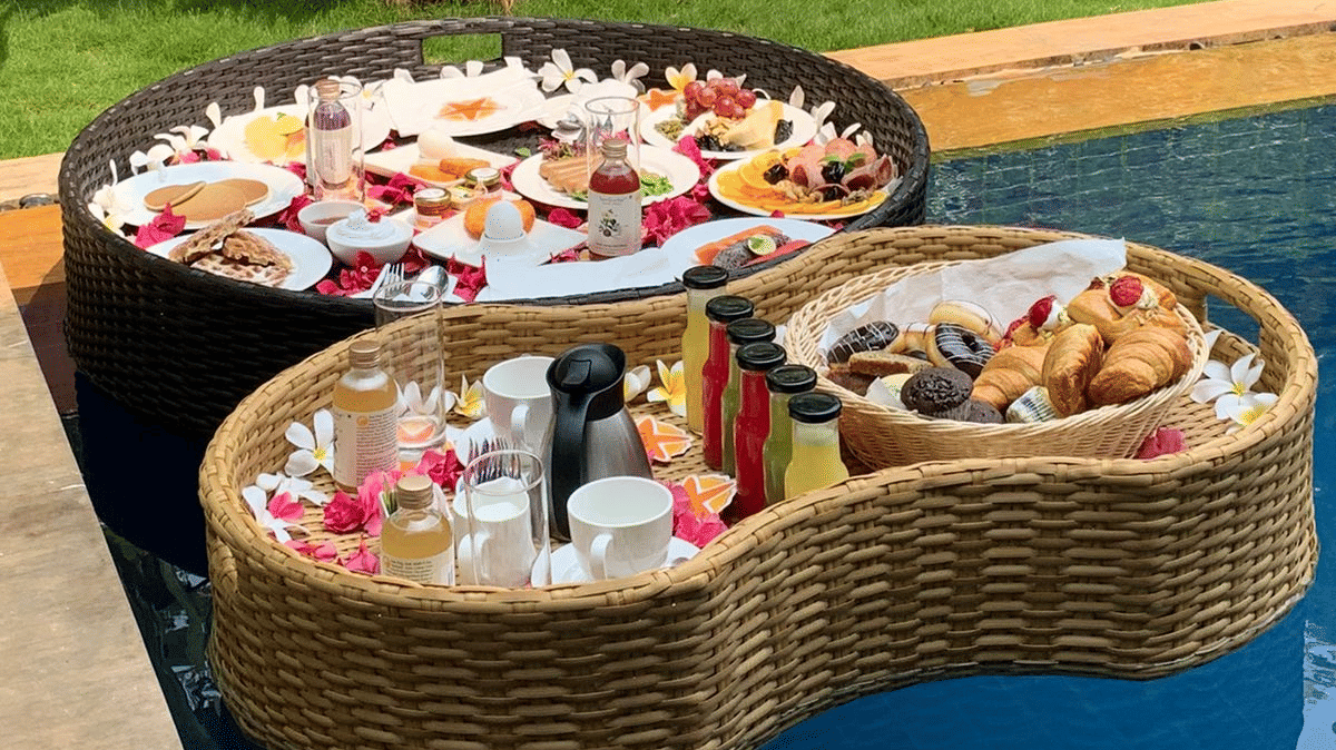 A close up of Two baskets filled with food, placed on the pool with blue loungers kept on the lawn area next to the pool at Azaya Beach Resort, Goa.