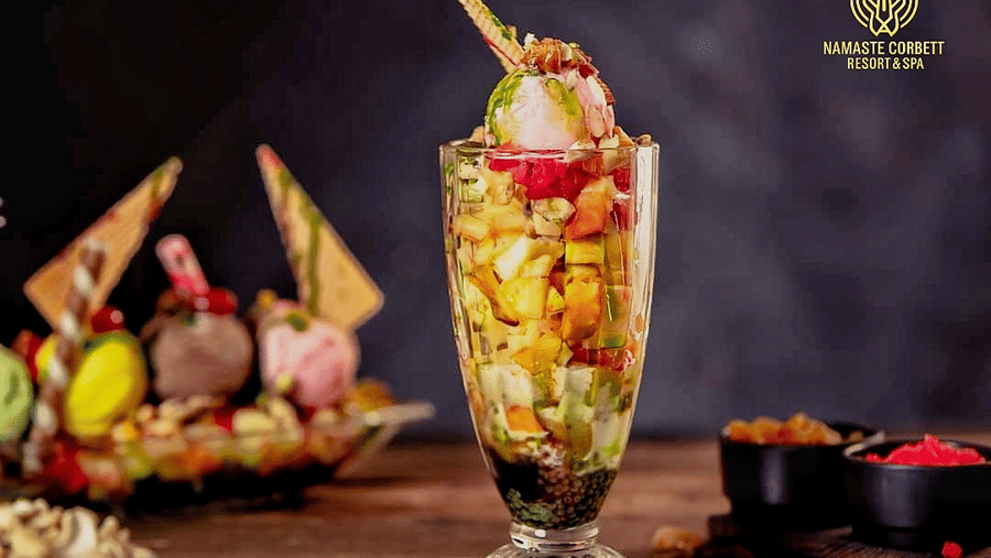 Tall layered fruit sundae topped with ice cream, fresh fruits, nuts, and wafer sticks served in a glass.