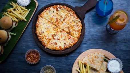 Top view of a table with various fast foods like pizza, fries, burgers, and dips, along with two drinks placed at Oriental Aster, Mumbai.