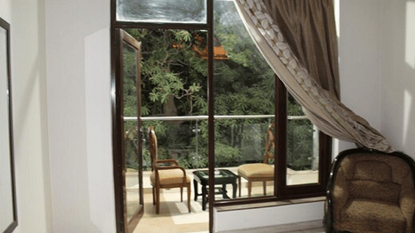 Large window opening to a private balcony with outdoor seating, elegant curtains and a bright, airy guest room ambience.