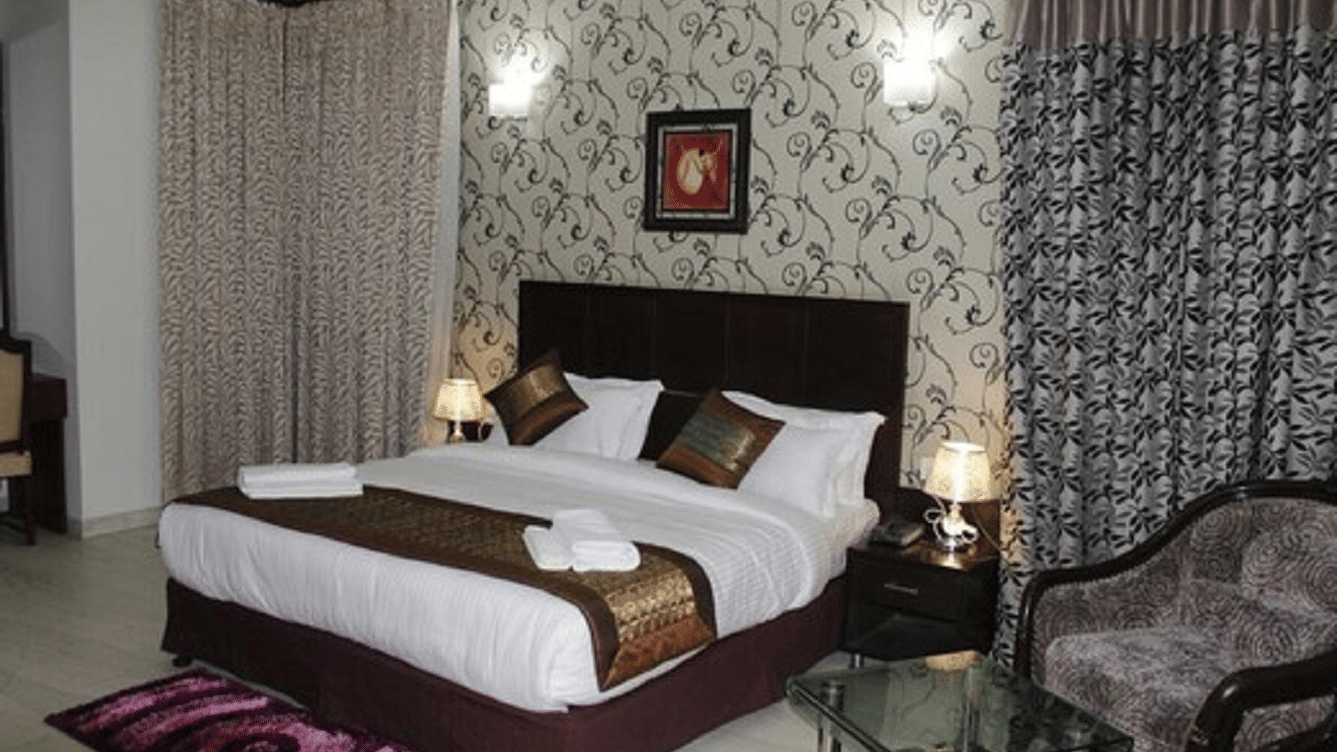 Double bed with a quilted headboard, white linen and a patterned accent wall.