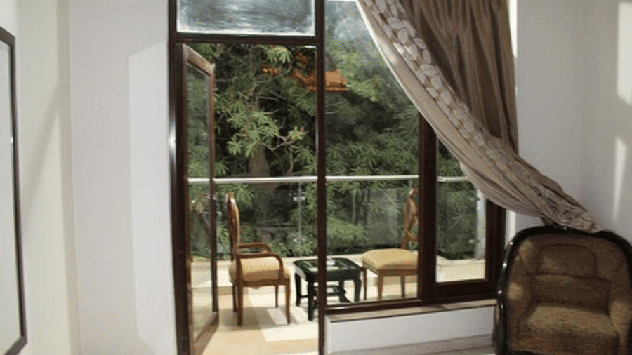 Large window opening to a private balcony with outdoor seating, elegant curtains and a bright, airy guest room ambience.