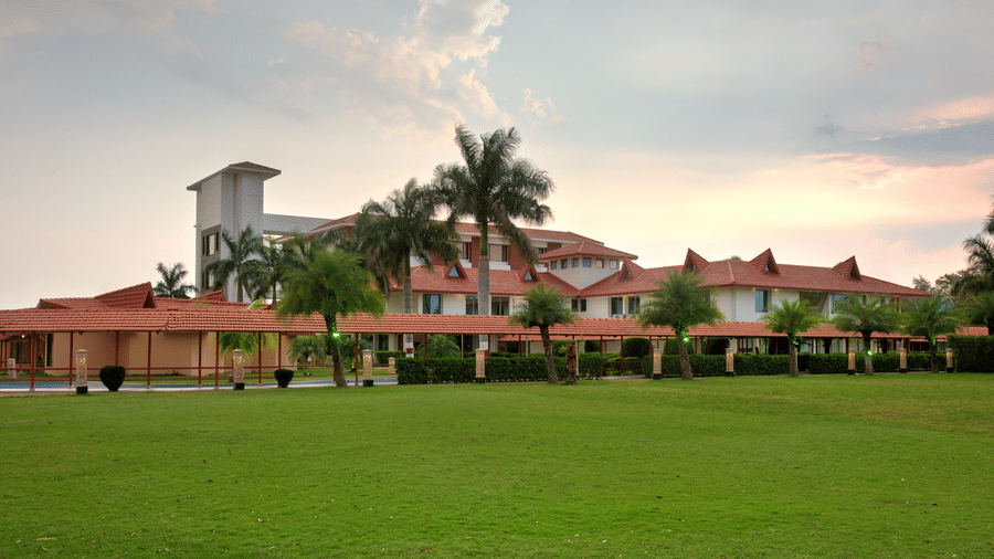 Exterior view showcasing lush grass and palm trees encircling the resort under a partly cloudy sky  | Crescent Spa & Resorts