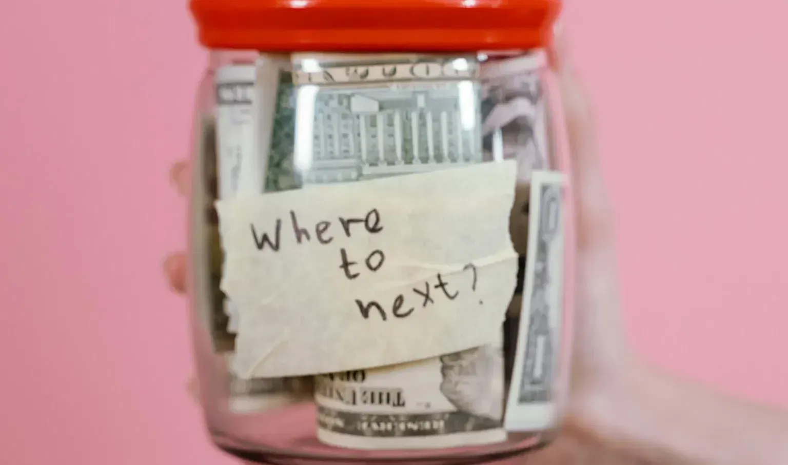 A glass jar filled with money and a handwritten note asking 'where to next?'.