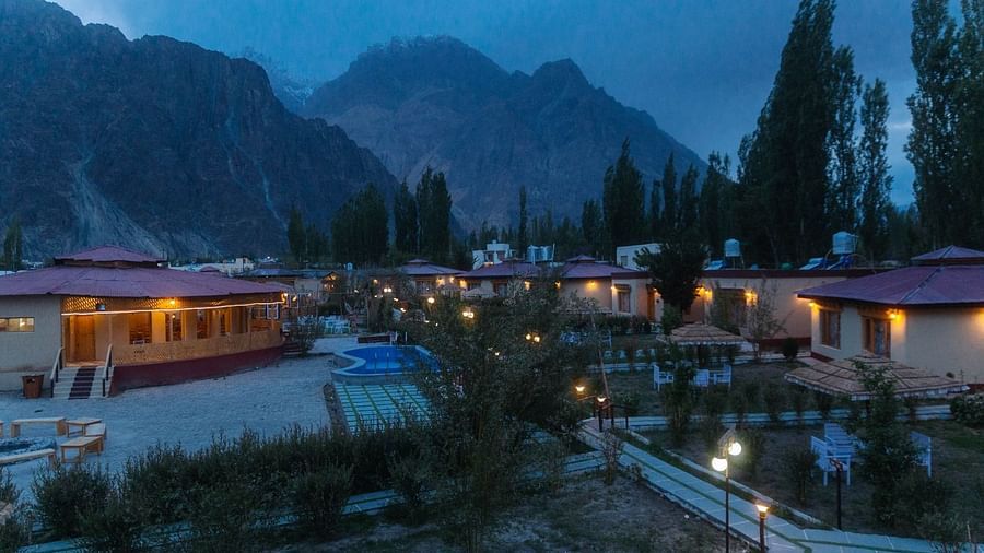 Aerial view of White Sand Resort, Ladakh at dusk, showing cabins, trees, and mountains under a cloudy sky.